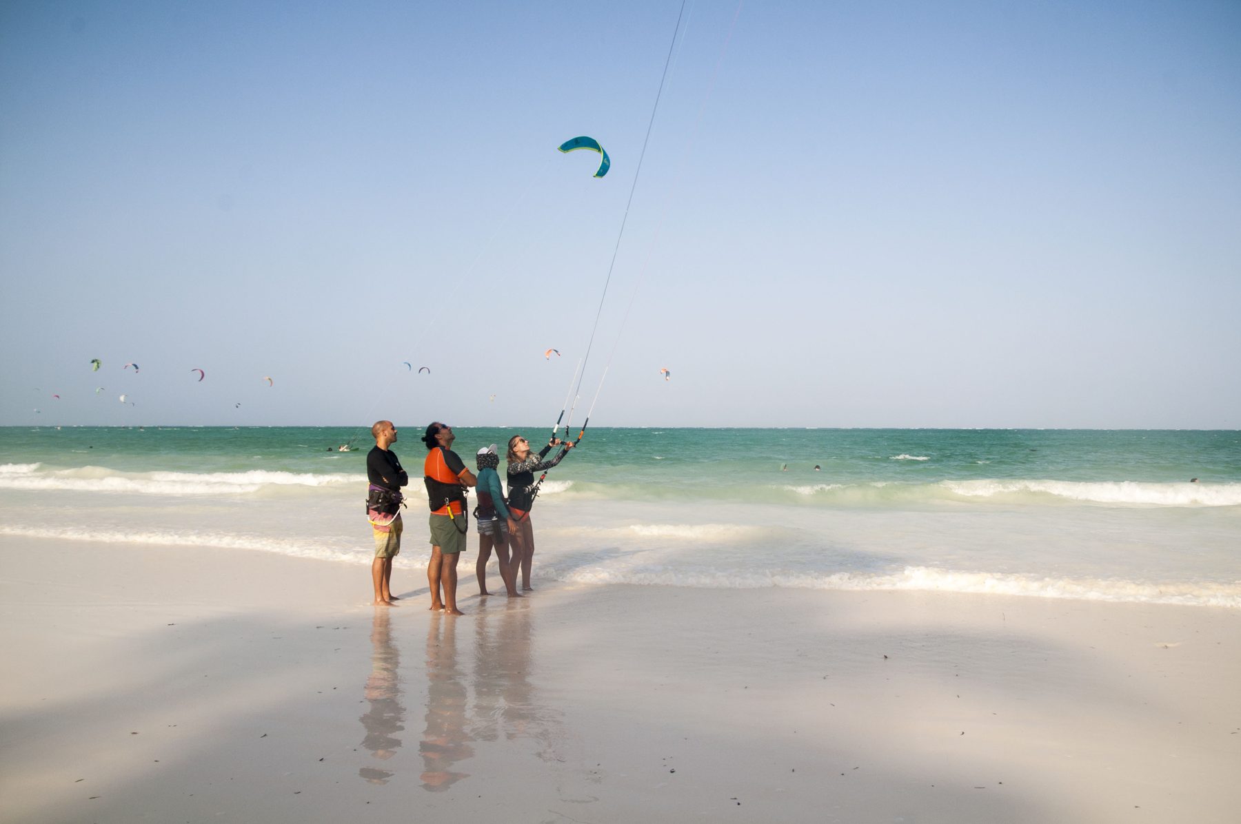 Travellers walking out across a wide, mirror-flat Zanzibar beach at low tide